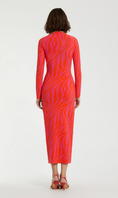 A person stands facing away, wearing the Mac Duggal Pink Casual Wedding-Guest Dress K12008, a long-sleeved, ankle-length zebra-print dress with red heeled sandals against a plain background.