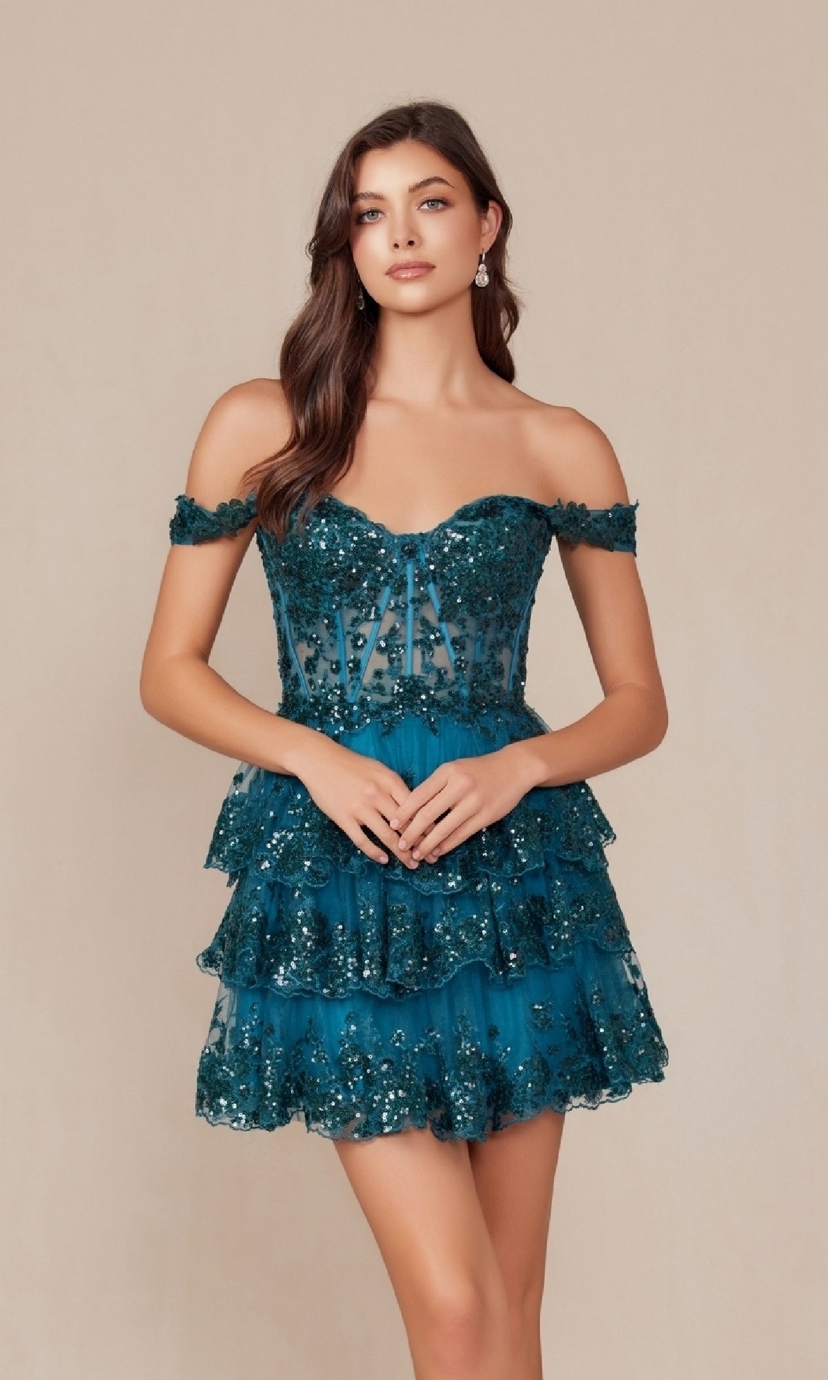 A woman models the Off-Shoulder Short Ruffled Sequin Hoco Dress K856 in teal, featuring tiered ruffles and sequin embellishments, standing against a plain beige background.
