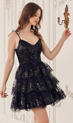 A woman stands indoors by a white ornate wall and brass sconce, wearing the Sequin-Print Short Ruffled Homecoming Dress KV1090—a black, sleeveless A-line dress with ruffles and sequin details.