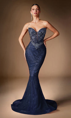 A woman wears the Ladivine KV1129 Strapless Long Mermaid Prom Gown in dark blue, featuring intricate beading and sheer details, as she stands against a plain brown background.