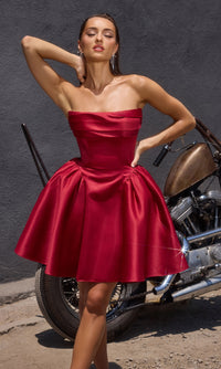 Woman in a burgundy red short strapless dress posing next to a motorcycle against a dark background