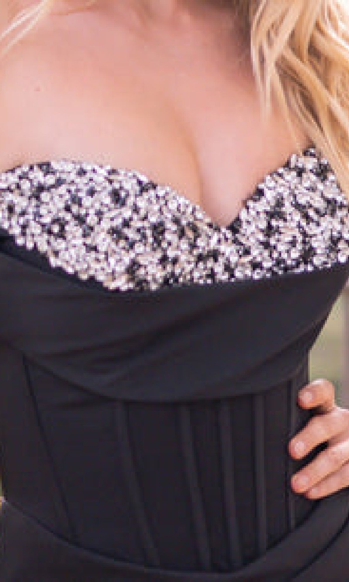 Someone wearing the Off-the-Shoulder Corset Prom Dress: Katrina by Velvi, featuring a black strapless silhouette and a sequined, silver-embellished neckline.