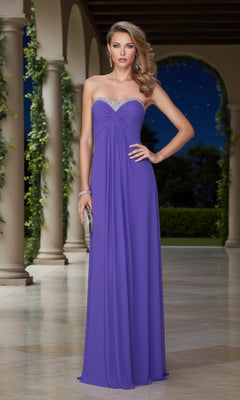 A woman wears the La Femme 21461 long prom dress, a strapless floor-length purple gown with silver details, standing at night in an elegant outdoor colonnade and holding a small clutch.