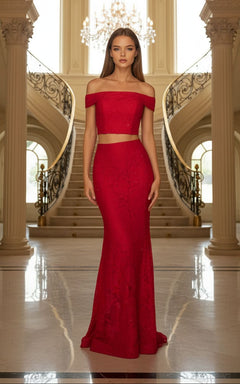 A woman stands indoors in the La Femme Two-Piece Mermaid Lace Prom Dress 27443, featuring a fitted silhouette and floor-length skirt in front of dual curved staircases and a chandelier.