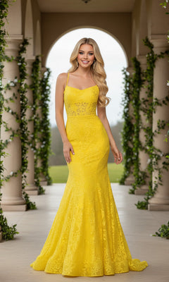 A woman stands outdoors between columns adorned with green vines, wearing the Long Lace Mermaid Prom Dress by La Femme in a vibrant yellow, floor-length style.