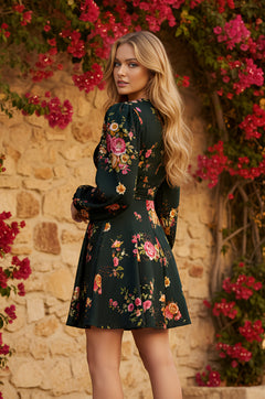 A woman wearing the Twilight Rose Short Casual Dress: Leah stands outdoors by a stone wall and blooming pink flowers, looking over her shoulder at the camera.