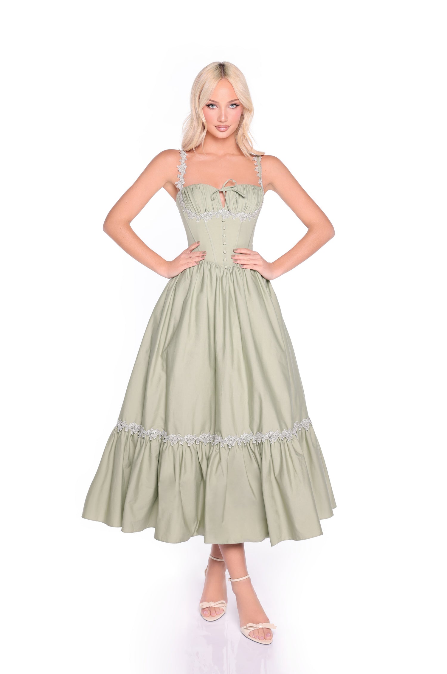 A woman faces forward wearing the Lioren Sage Green Casual Midi Dress, featuring a corset bodice, ruffled skirt, lace-up back, and paired with light sandals.