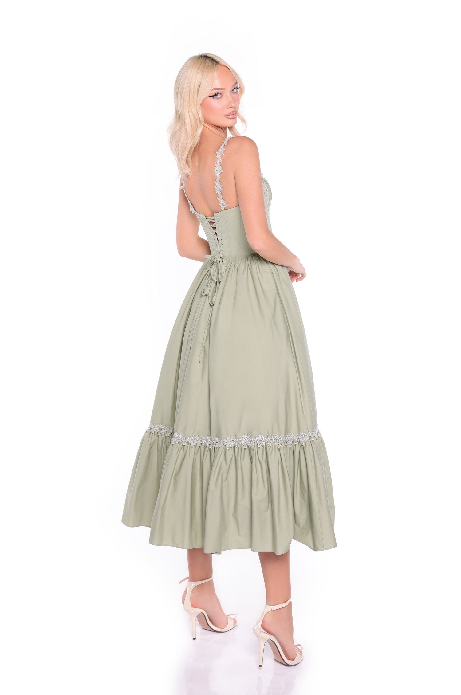 Woman wearing the Lioren Sage Green Casual Midi Dress with a lace-up back, lace trim, fitted corset bodice, and flared skirt. She pairs it with high-heeled sandals and looks over her shoulder.