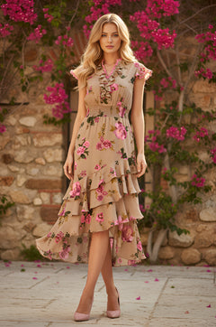 A woman in the Taupe Pink Floral Midi Wedding-Guest Dress: Lucy stands outdoors by a stone wall with blooming pink flowers and greenery.