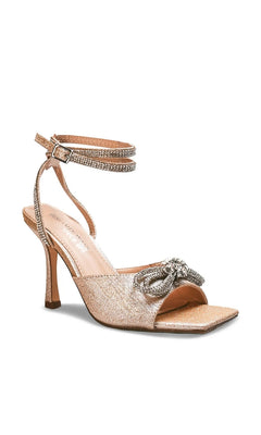 Lux Champagne Stiletto Prom Shoes: Touch Ups 4742, a champagne-colored glittery stiletto sandal featuring a rhinestone-embellished bow on the toe and a crystal-studded ankle strap.