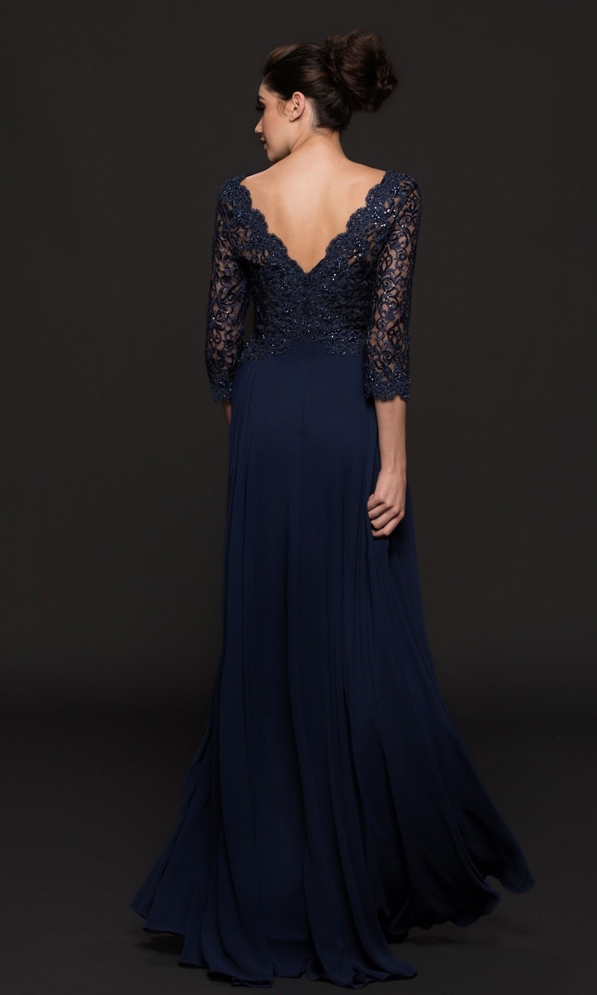 Woman facing away in the Long Sleeve Mother-of-the-Bride Gown: Marsoni M225, a navy floor-length gown with lace sleeves and V-back, set against a black background.