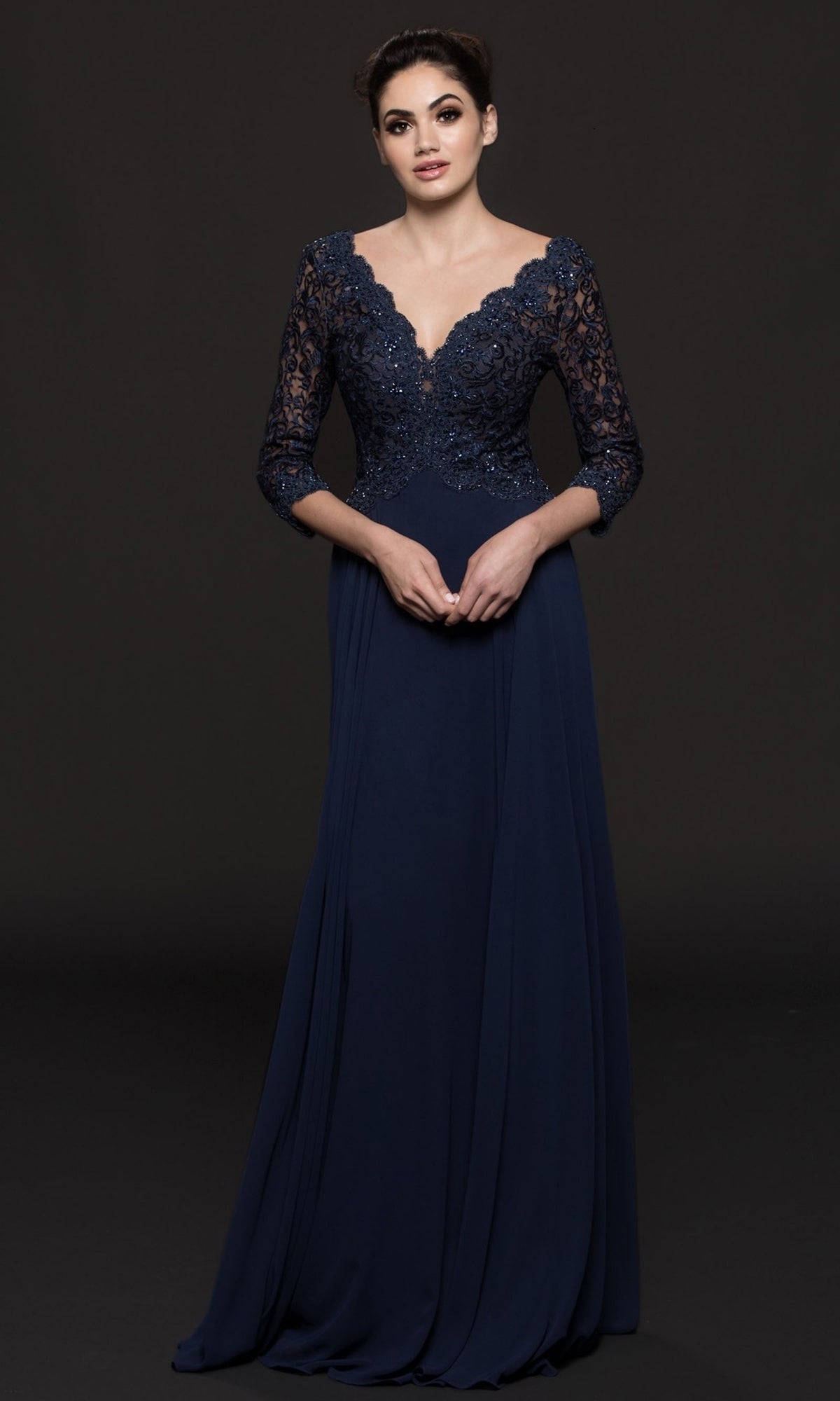 Woman in the Long Sleeve Mother-of-the-Bride Gown: Marsoni M225, featuring navy lace sleeves and a scalloped V-neckline, posed against a dark background.