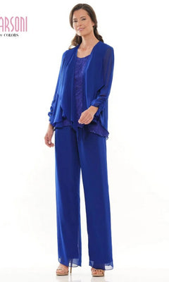 A woman smiles in the Marsoni M303 Long Formal Pantsuit in sapphire, featuring a layered chiffon jacket, sleeveless lace top, wide-leg trousers, and beige heels.