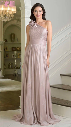 A woman stands indoors near a staircase, gracefully wearing the Marsoni M332 Long Formal Dress in light mauve—a floor-length, one-shoulder chiffon evening gown with a 3D floral embellishment on the strap.