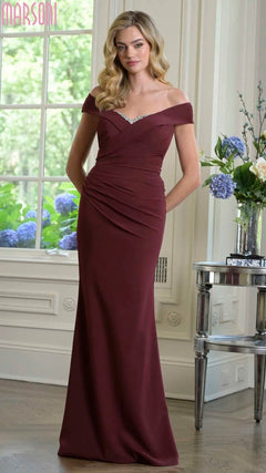 A woman stands indoors wearing the Marsoni M342 long formal dress in wine, an off-the-shoulder gown with jeweled detailing at the neckline.