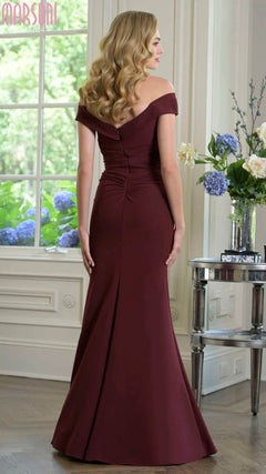 A woman with long wavy blonde hair wears the Marsoni M342 long formal dress in floor-length burgundy stretch crepe, standing indoors and facing away from the camera.