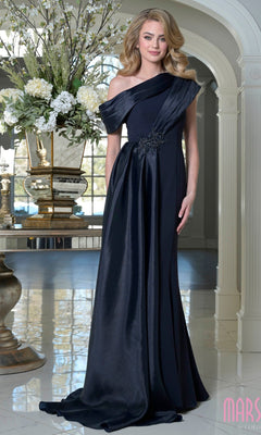 A woman in an asymmetrical navy Marsoni M346 long formal dress stands in an elegant room filled with floral arrangements and decorative vases.