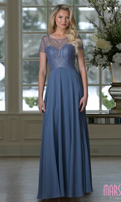 A woman wears the Marsoni M351, a slate blue floor-length chiffon A-line gown with short sleeves and a sheer beaded bodice, perfect as an elegant mother-of-the-bride dress. Large floral arrangements and tall windows are behind her.