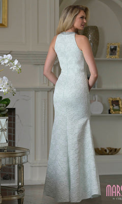 A woman stands indoors facing away, wearing the Marsoni M356 long formal dress in light blue floral jacquard with a high neckline.