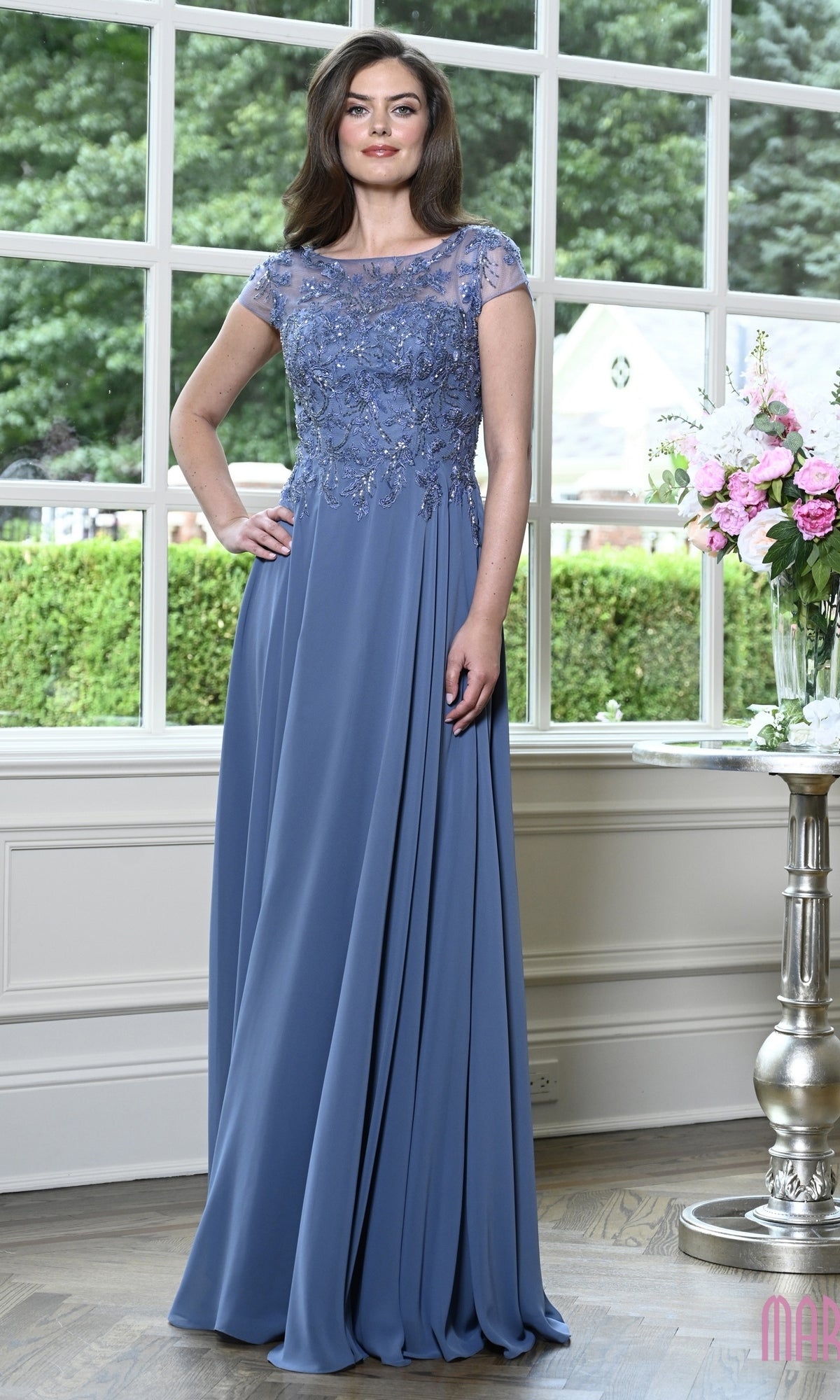 A woman wearing a slate blue Modest Long Formal Dress: Marsoni M360, featuring an A-line silhouette with a beaded, cap-sleeved bodice and a flowing floor-length skirt.