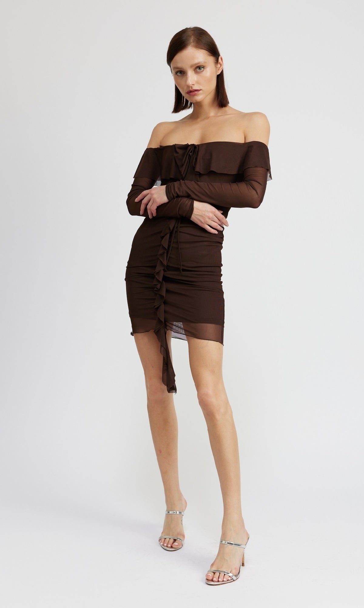A woman poses against a plain background wearing the Chocolate Brown Short Party Dress with Sleeves featuring an off-the-shoulder neckline, ruched details, and clear high-heeled sandals.