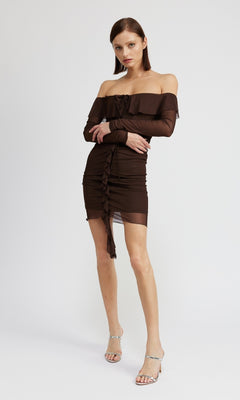 A woman poses against a plain background wearing the Chocolate Brown Short Party Dress with Sleeves featuring an off-the-shoulder neckline, ruched details, and clear high-heeled sandals.