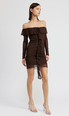 A woman models the Chocolate Brown Short Party Dress with Sleeves, featuring an off-the-shoulder design and ruffle details, paired with silver high-heeled sandals against a plain white background.