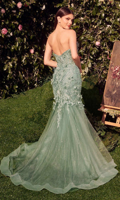 A woman in the Andrea & Leo MA101 long sleeve long formal dress stands on grass before leafy shrubs and an easel with a painting, the gown's tulle train flowing behind her.