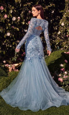 A woman in the Andrea & Leo MA101 long sleeve long formal dress with a beaded lace bodice and flowing tulle train stands outdoors by a bush with pink and white flowers.
