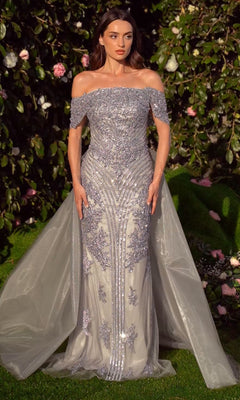 A woman in the Long Silver Prom Ball Gown: Andrea & Leo MA103, featuring ornate beadwork and a sheer train, stands before lush greenery and pink flowers.