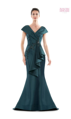 A woman wearing the Marsoni MV1086 long formal dress in deep green, featuring an off-the-shoulder neckline, floor-length trumpet silhouette, floral embellishments, and cascading front ruffle detail.