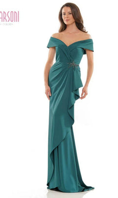 A woman wearing the Marsoni MV1180 Long Formal Dress in forest, featuring an off-the-shoulder neckline, decorative brooch, beaded waistline, and ruffled drape detail, stands against a plain white background.