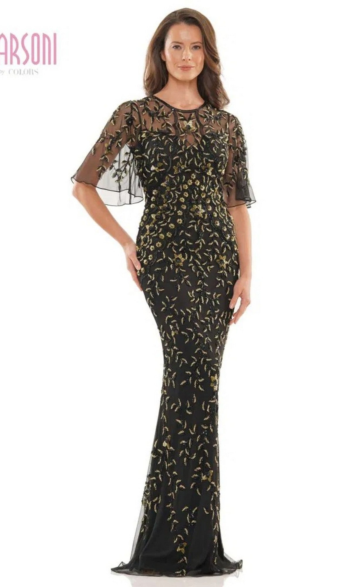 A woman poses against a plain background in the Marsoni MV1208 long formal dress, a black gold gown with a fitted sheath silhouette, sheer short sleeves, and elegant gold embroidered floral patterns.