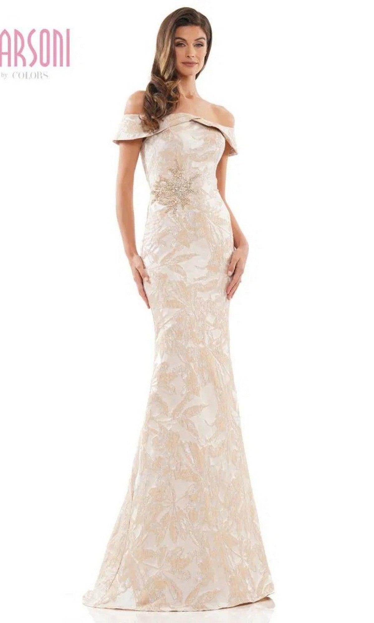 A woman wears the Marsoni MV1223 long formal dress in gold, a fitted, floor-length gown with off-the-shoulder design and floral embellishments, standing against a plain white background.