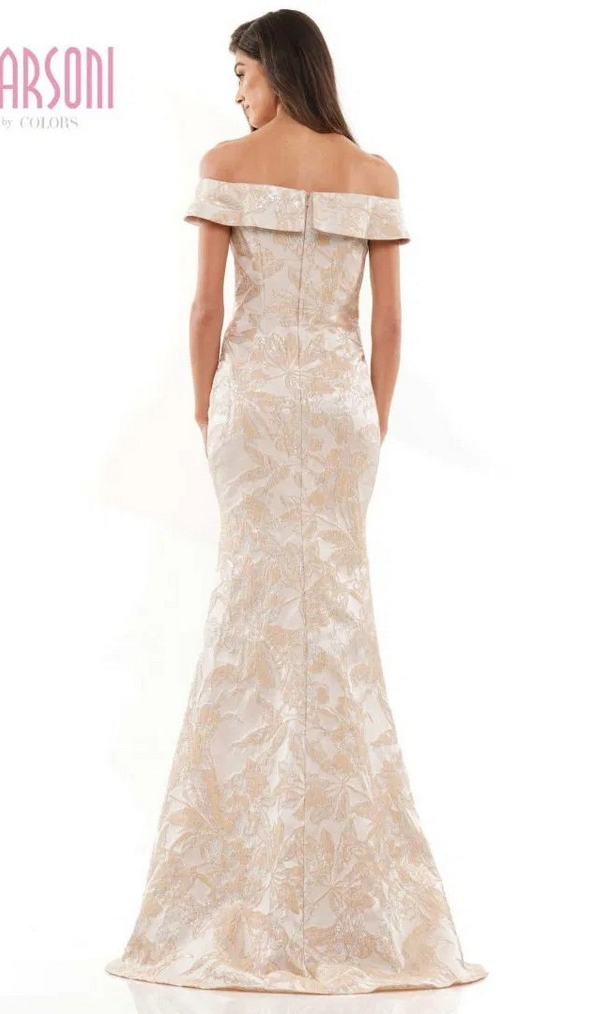A woman stands gracefully with her back to the camera, wearing the Marsoni MV1223 long formal dress—an off-the-shoulder, floor-length gown featuring a light floral pattern and a fitted silhouette.