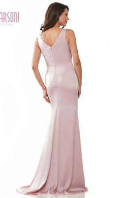 A woman stands facing away, wearing the Marsoni MV1233—a long formal dress in light pink with a sleeveless design, V-shaped back, and draped faille fabric.