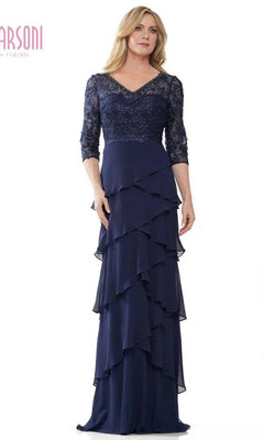 A woman stands against a white background wearing the Marsoni MV1244 long formal dress in navy, featuring a lace embroidered bodice, three-quarter sleeves, and a layered ruffle skirt.