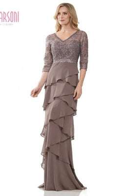 A woman stands against a white background wearing the Marsoni MV1244 long formal dress in taupe, featuring lace sleeves, a lace embroidered bodice, and a tiered ruffled chiffon column skirt.