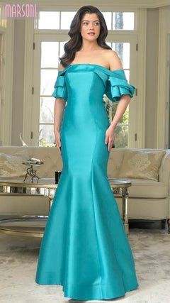 A woman poses indoors in the Marsoni MV1290 long formal dress, featuring an off-the-shoulder fitted mermaid silhouette with ruffled sleeves in Tiffany color, standing before large windows and neutral-toned furniture.