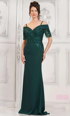 A woman in the Marsoni MV1295 long formal dress in deep green, featuring sequin appliques, off-the-shoulder sleeves, and spaghetti straps, stands against a white ornate background.