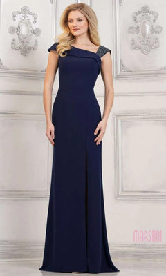 A woman stands in an elegant room, wearing the navy Long Formal Dress: Marsoni MV1296—a floor-length crepe gown with beaded detailing on one shoulder.