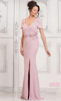 A woman wearing the Marsoni MV1297 Long Formal Dress in rose, featuring short sleeves, floral embroidery at the waist, a crepe floor-length skirt, and front slit stands in an elegant room with white paneled walls.