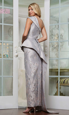 A woman stands indoors wearing the Marsoni MV1300, a silver jacquard long formal dress with an asymmetrical peplum waist, paired with high heels and facing slightly away from the camera.