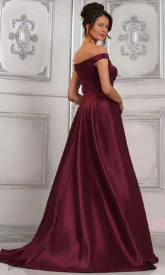 Wearing the Marsoni MV1310, a long formal off-the-shoulder mermaid gown, a woman stands in an elegantly decorated room, gazing over her shoulder.