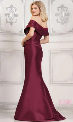 A woman in the Marsoni MV1312 long formal dress—a stretch Mikado, off-shoulder, floor-length gown with a mermaid skirt—stands in a white, ornately decorated room, facing slightly away from the camera.