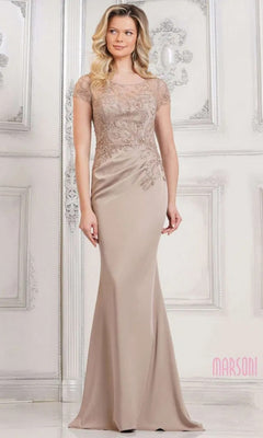 A woman stands in an elegant room wearing the Marsoni MV1317 long formal dress in taupe, featuring a beaded-embellished bodice and lace cap sleeves.