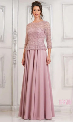 A woman wears the Marsoni MV1319 long formal dress in rose, featuring an elegant lace bodice, three-quarter sleeves, and a graceful A-line skirt, as she stands before a white paneled wall.