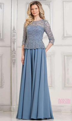 A woman in the Marsoni MV1319 long formal dress, featuring a beaded bodice, three-quarter sleeves, and an elegant slate blue A-line skirt, stands before an ornate white wall.