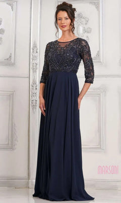 A woman stands indoors wearing the Marsoni MV1322 long formal dress in navy, featuring a lace embroidered bodice, three-quarter sleeves, and a flowing chiffon pleated skirt.