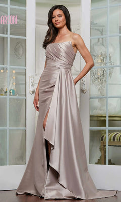 A woman stands indoors wearing the Marsoni MV1326 long formal dress in taupe, featuring a one-shoulder design, pleated detailing, and a thigh-high slit.